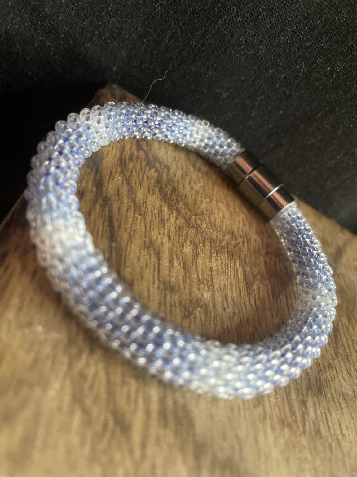 Handgefertigtes Glasperlenarmband in Eisblau und Weiß mit Magnetverschluss auf schwarzem Hintergrund
