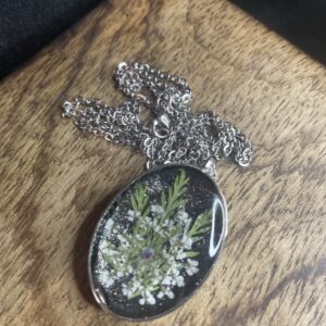 Handgefertigte Blumen-Halskette mit ovalem Resin-Anhänger und echten weißen Blüten auf schwarzem Hintergrund