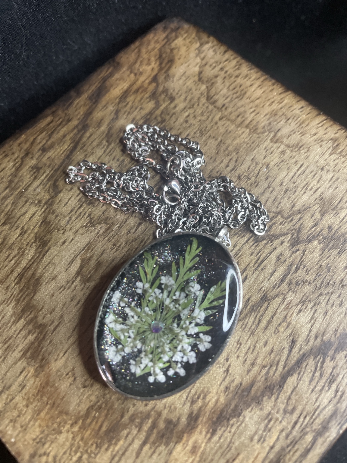 Handgefertigte Blumen-Halskette mit ovalem Resin-Anhänger und echten weißen Blüten auf schwarzem Hintergrund