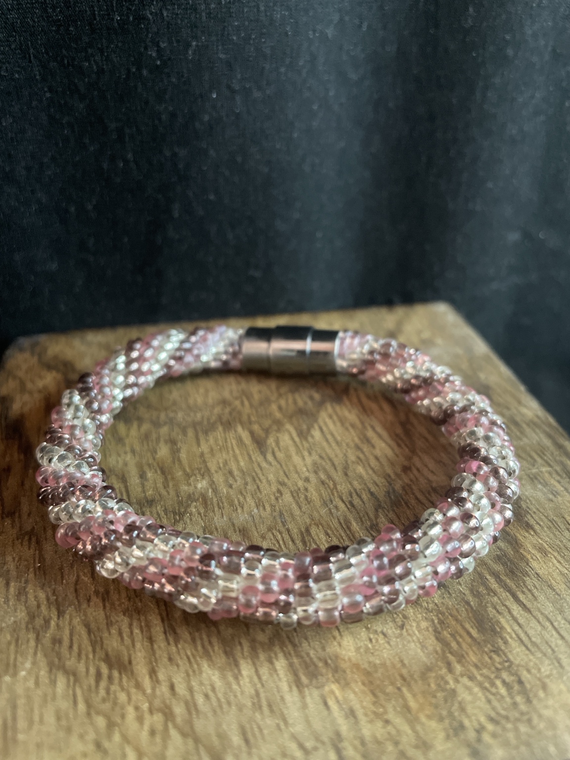 Handgefertigtes Glasperlenarmband in Rosé und Transparent mit Magnetverschluss auf schwarzem Hintergrund