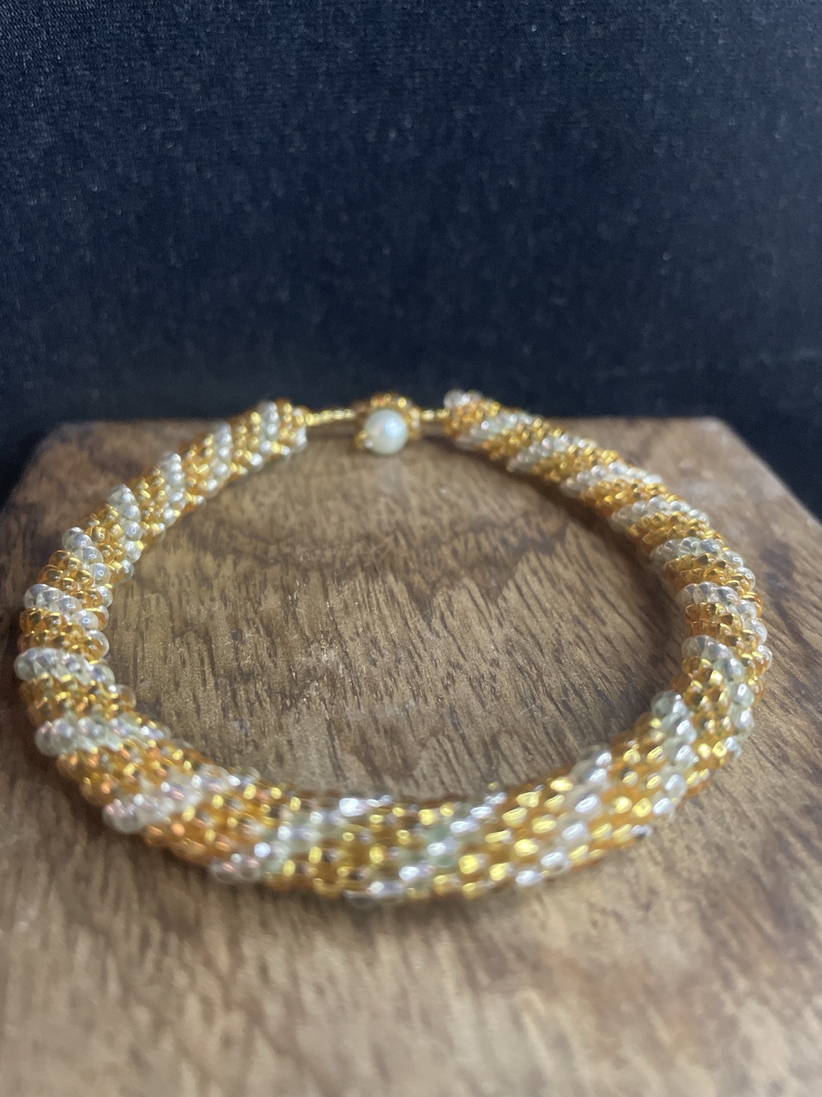 Handgefertigtes Glasperlenarmband in Gold und Weiß mit Knebelverschluss auf schwarzem Hintergrund