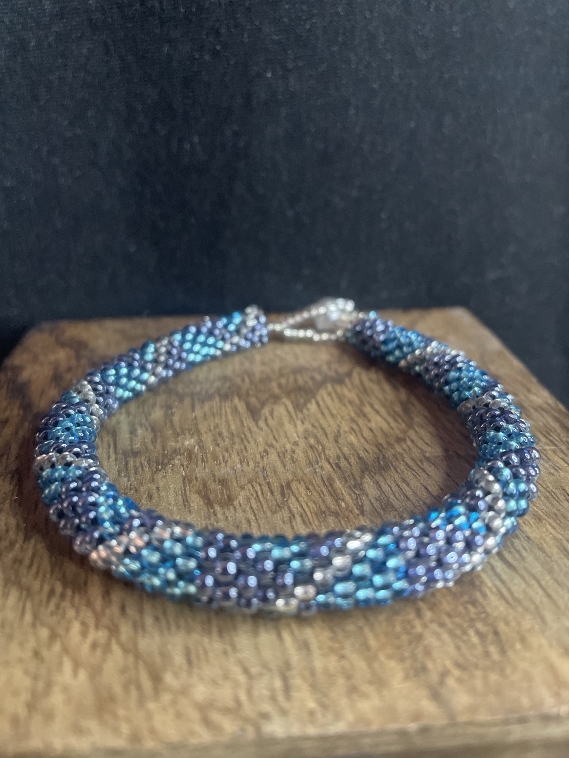 Handgefertigtes Glasperlenarmband in Blau, Türkis und Silber mit Knebelverschluss auf schwarzem Hintergrund