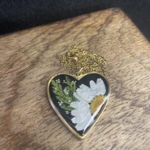 Goldene Herz-Halskette mit echter Margerite im Resin auf schwarzem Hintergrund