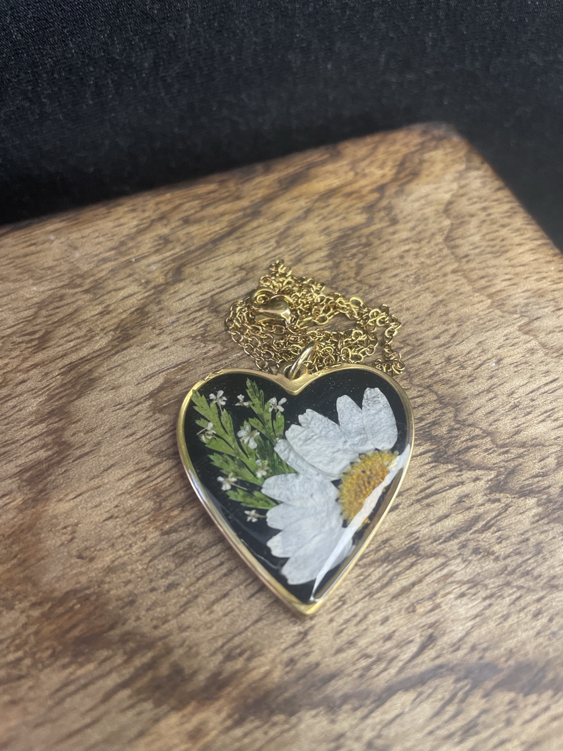 Goldene Herz-Halskette mit echter Margerite im Resin auf schwarzem Hintergrund