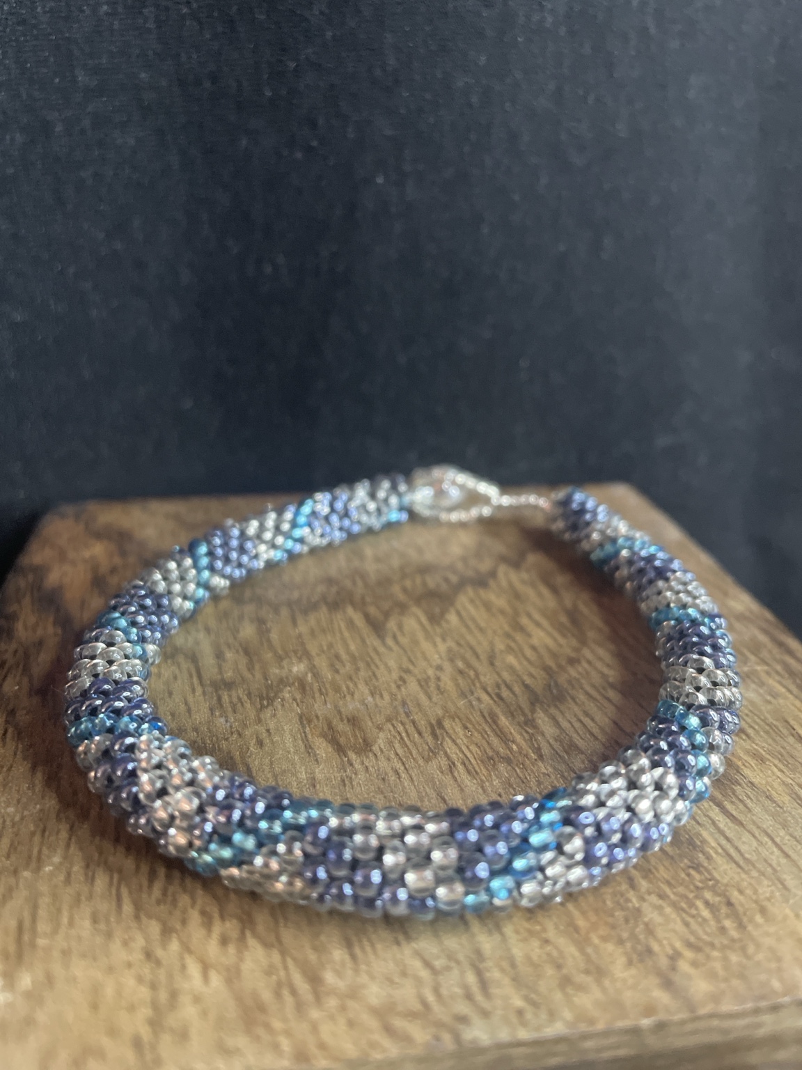 Handgefertigtes Glasperlenarmband in Blau und Silber mit Knebelverschluss auf schwarzem Hintergrund