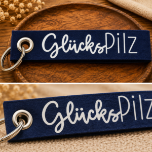 Dunkelblauer Filz-Schlüsselanhänger mit Glückspilz Schriftzug auf dekorativem Holztablett