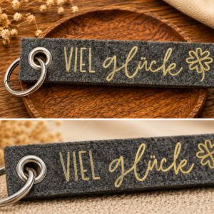 Grauer Filz-Schlüsselanhänger mit Viel Glück Schriftzug und Kleeblatt Motiv auf Holztablett