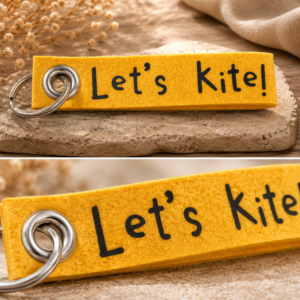 Gelber Filz-Schlüsselanhänger mit Let’s Kite Schriftzug auf dekorativem Untergrund