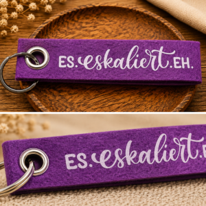 Lila Filz-Schlüsselanhänger mit Schriftzug Es eskaliert eh auf dekorativer Holzschale