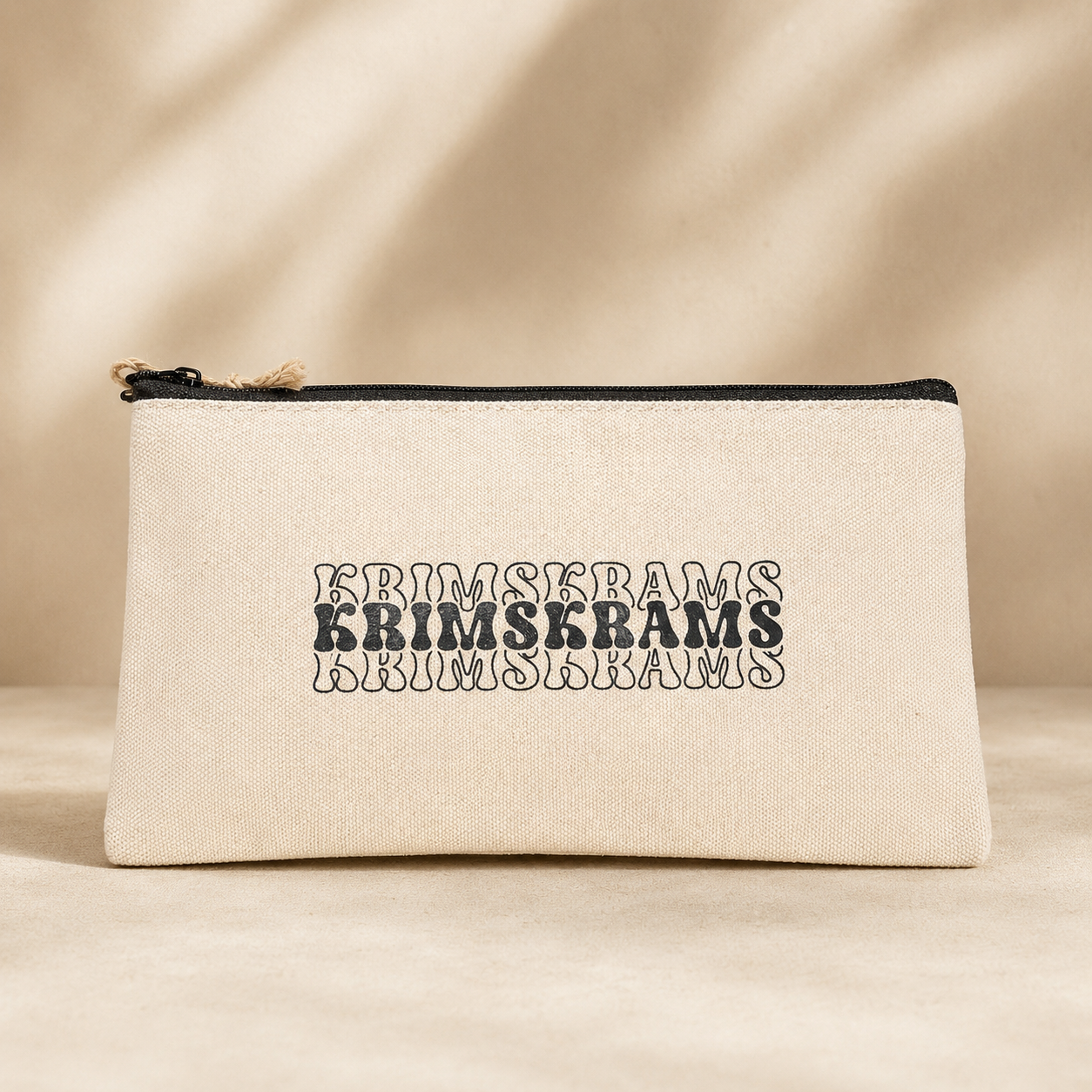 Naturfarbene Kosmetiktasche mit schwarzem Rei&szlig;verschluss und Retro-Aufdruck &bdquo;KRIMSKRAMS&ldquo; auf hellem Hintergrund.