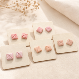 Handgefertigte Origami-Ohrstecker in verschiedenen Rosa- und Roséfarben auf hellen Schmuckkarten dekorativ präsentiert.