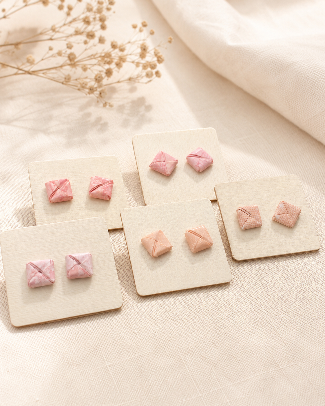 Handgefertigte Origami-Ohrstecker in verschiedenen Rosa- und Roséfarben auf hellen Schmuckkarten dekorativ präsentiert.