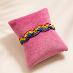 Handgeknüpftes Regenbogen-Armband mit bunten Farbakzenten auf rosa Schmuckkissen.