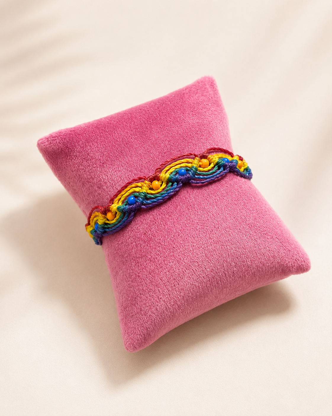 Handgeknüpftes Regenbogen-Armband mit bunten Farbakzenten auf rosa Schmuckkissen.
