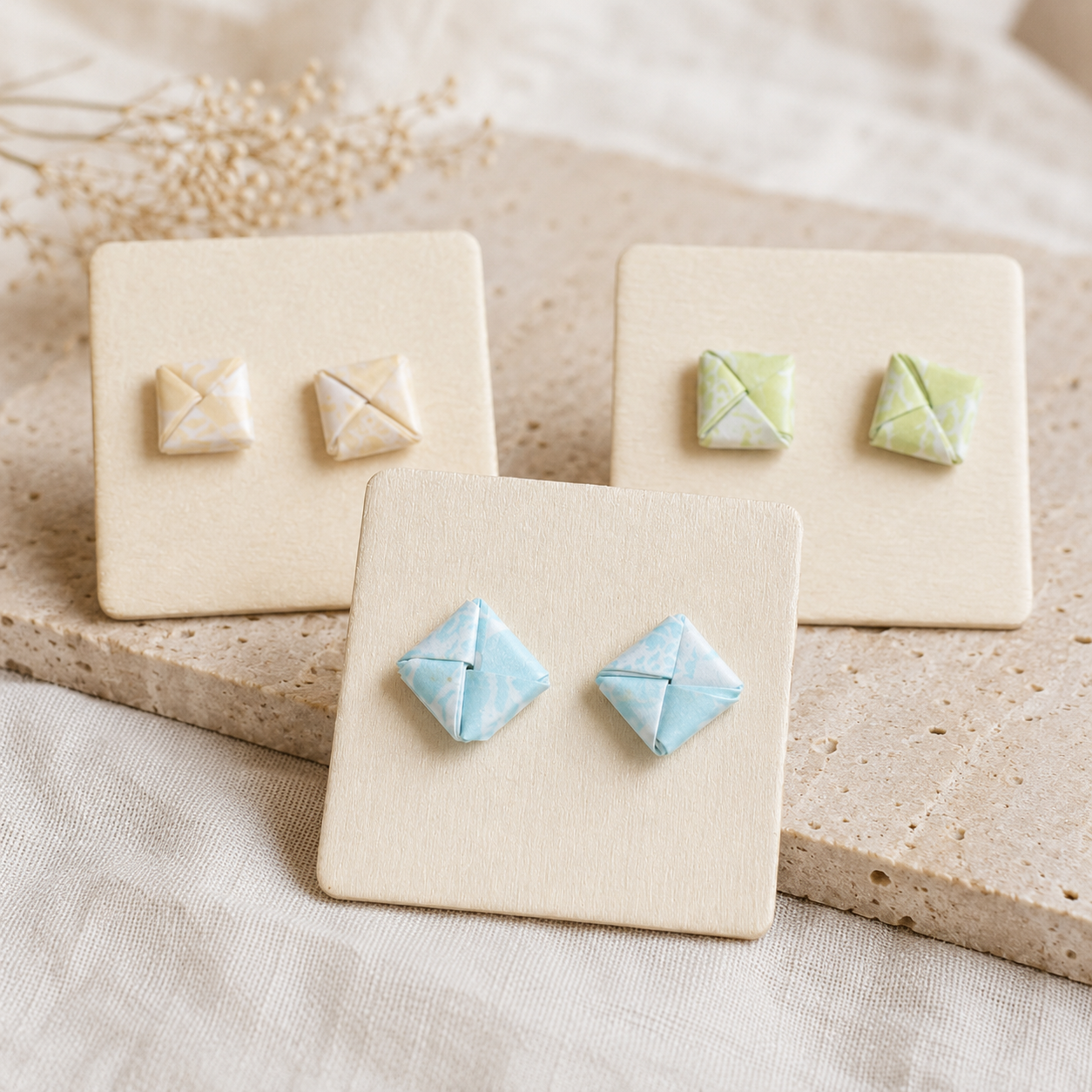 Handgefertigte Origami-Ohrstecker in Creme, Mintgrün und Hellblau auf dekorativen Schmuckkarten.