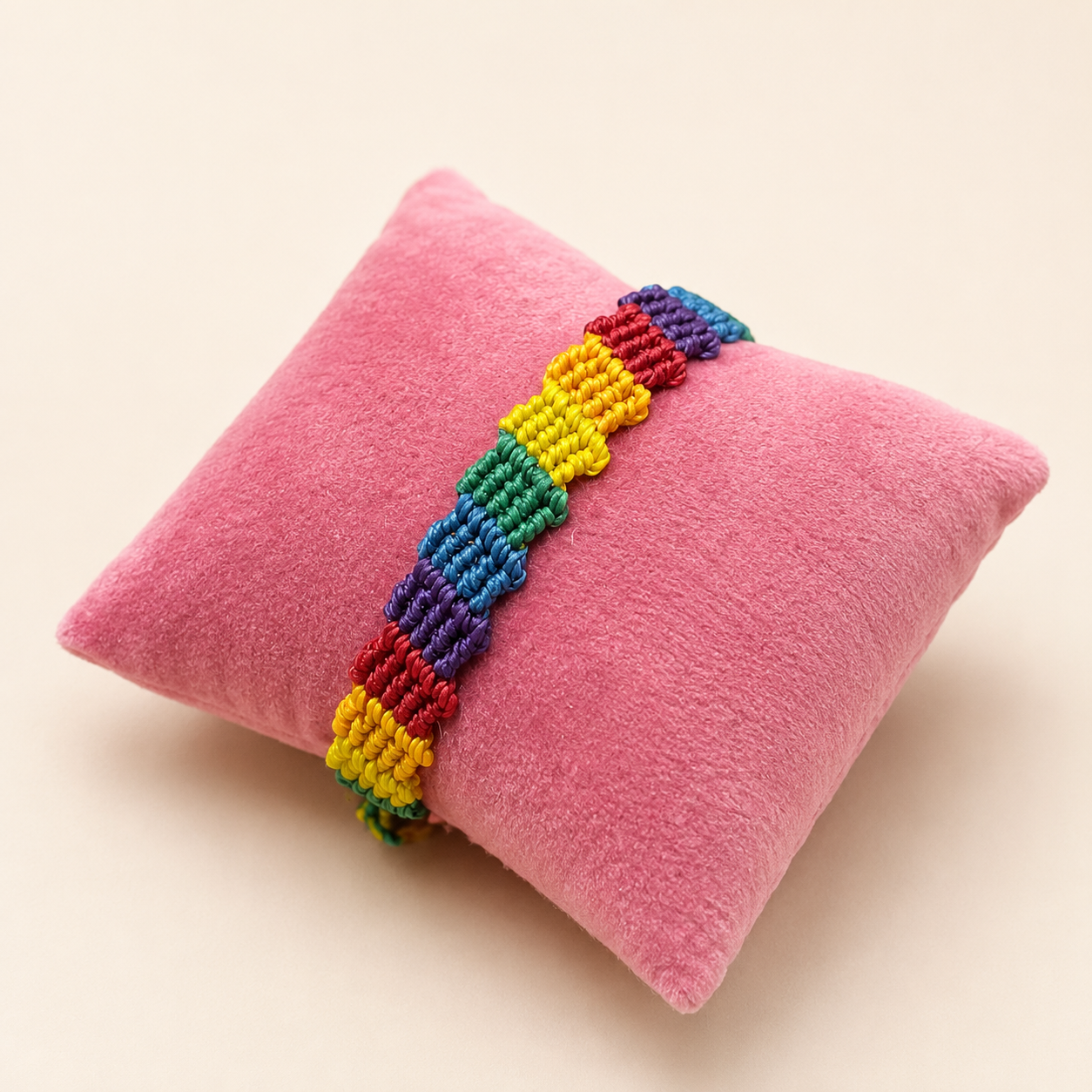 Handgeknüpftes buntes Makramee-Armband ohne Perlen in Regenbogenfarben auf rosafarbenem Schmuckkissen.