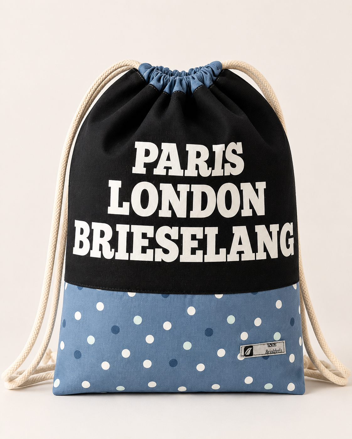 Handgefertigter Turnbeutel aus Stoff mit schwarzem Oberteil, hellblauem Punktedesign und dem Aufdruck „Paris London Brieselang“.