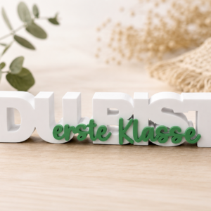 3D-gedruckter weißer Schriftzug „Du bist“ mit grünem Schriftzug „erste Klasse“ als freistehende Dekoration zur Einschulung.