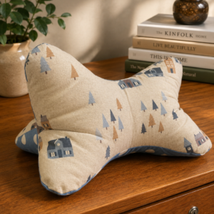 Leseknochen aus hellem Stoff mit blau-grauem Waldmotiv, kleinen Häusern und Tannenbäumen.