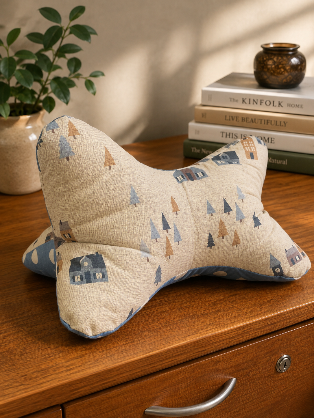 Leseknochen aus hellem Stoff mit blau-grauem Waldmotiv, kleinen Häusern und Tannenbäumen.