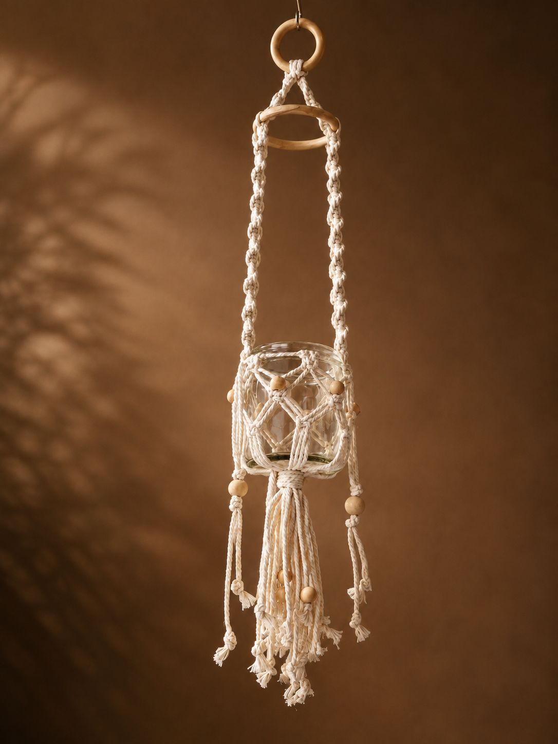 Handgeknüpftes Makramee Windlicht zum Aufhängen mit Glas und Holzperlen im natürlichen Boho-Stil.